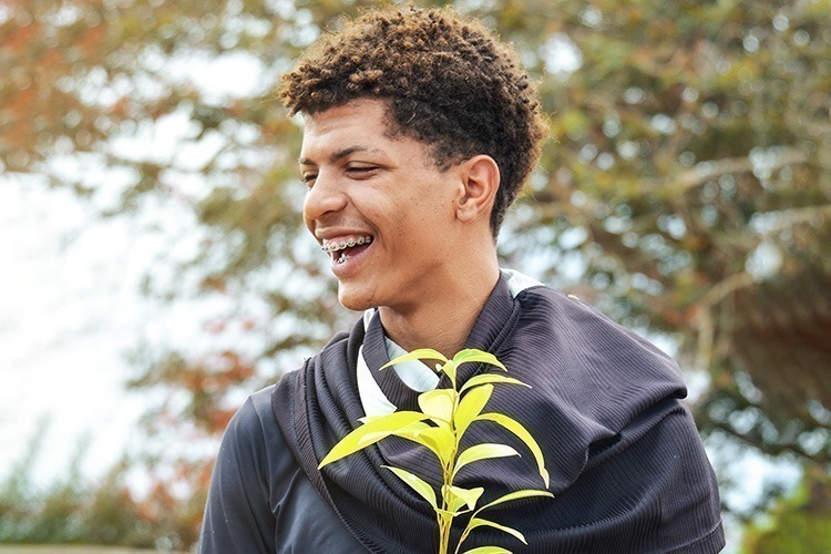 Jovem sorrindo segurando uma planta.