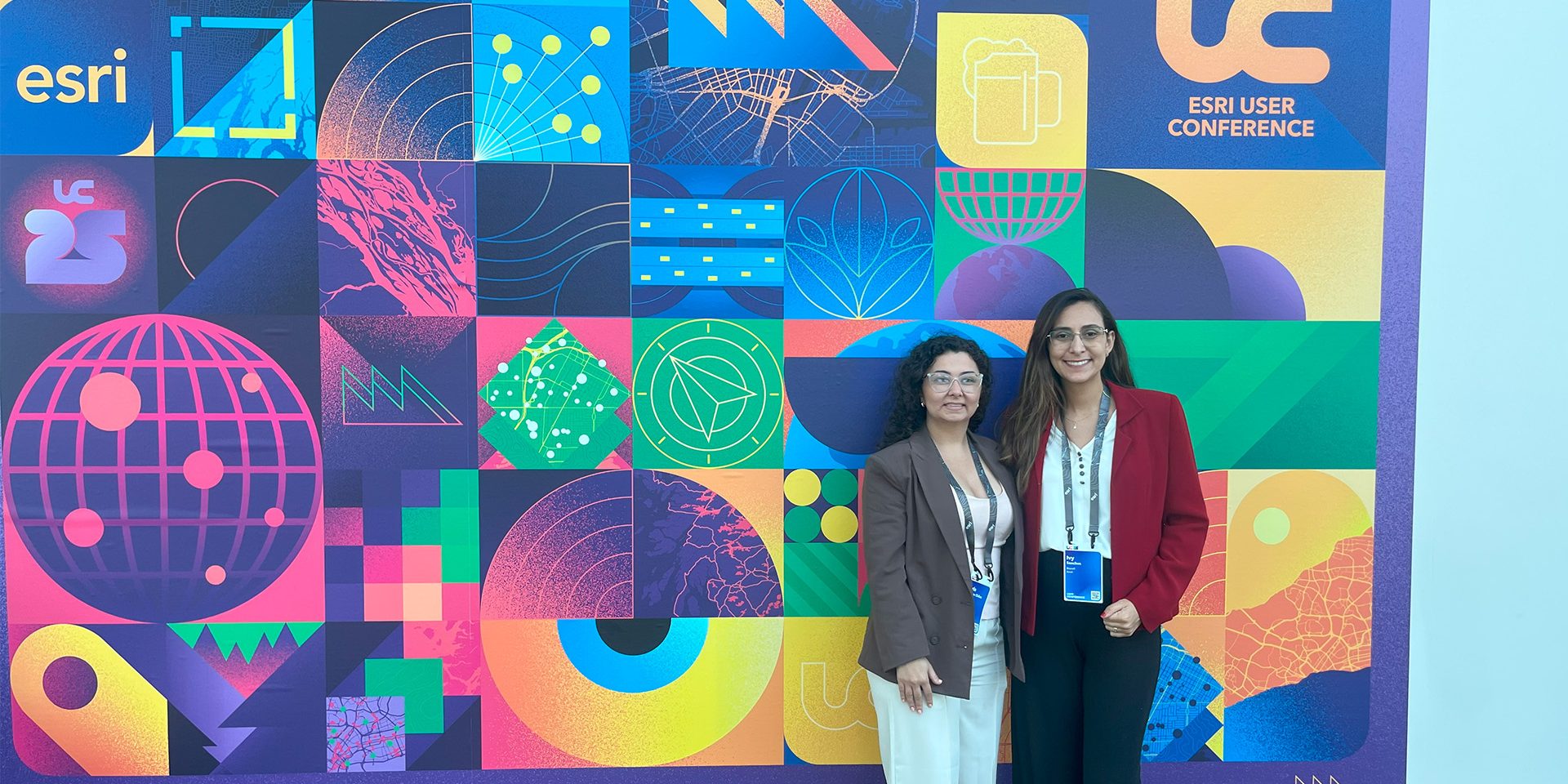 Ivy e Carla em frente ao painel do evento Esri UC