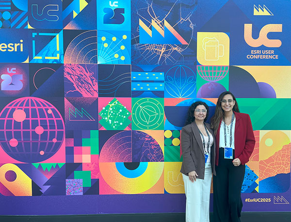 Ivy e Carla em frente ao painel do evento Esri UC