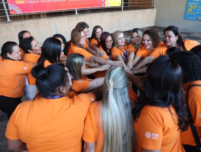 Group of participants wearing orange shirts standing in a circle with hands joined at the center during the Dona Della 2024 closing ceremony.