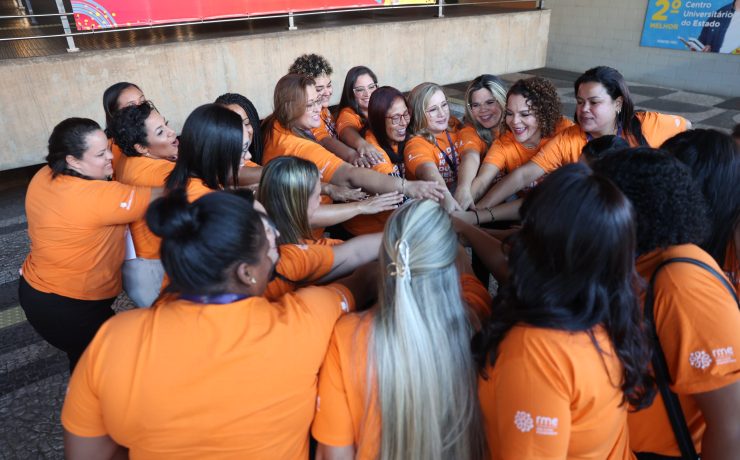 Group of participants wearing orange shirts standing in a circle with hands joined at the center during the Dona Della 2024 closing ceremony.