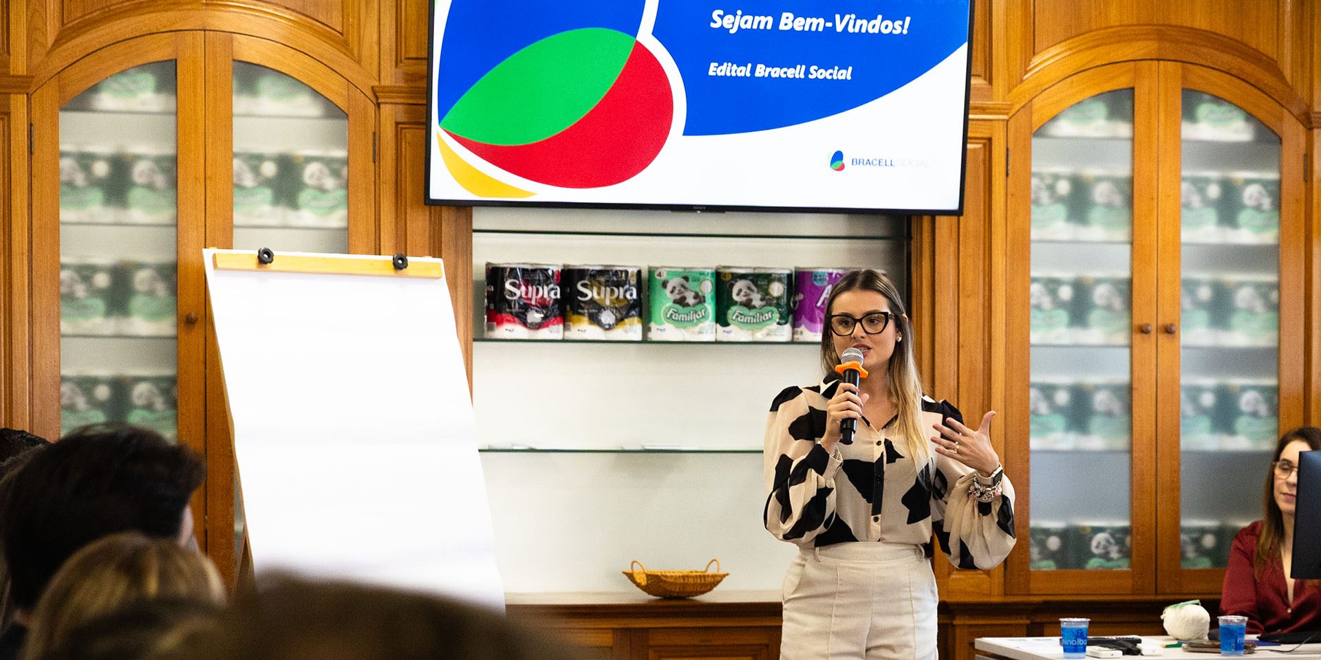 Pessoa faz apresentação durante evento do Edital Bracell Social em uma sala de reuniões. Ao fundo, uma tela exibe a mensagem “Sejam Bem-Vindos! Edital Bracell Social”, enquanto participantes acompanham a atividade.