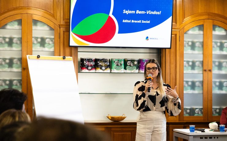 Pessoa faz apresentação durante evento do Edital Bracell Social em uma sala de reuniões. Ao fundo, uma tela exibe a mensagem “Sejam Bem-Vindos! Edital Bracell Social”, enquanto participantes acompanham a atividade.