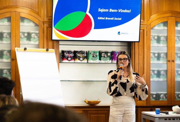 Pessoa faz apresentação durante evento do Edital Bracell Social em uma sala de reuniões. Ao fundo, uma tela exibe a mensagem “Sejam Bem-Vindos! Edital Bracell Social”, enquanto participantes acompanham a atividade.