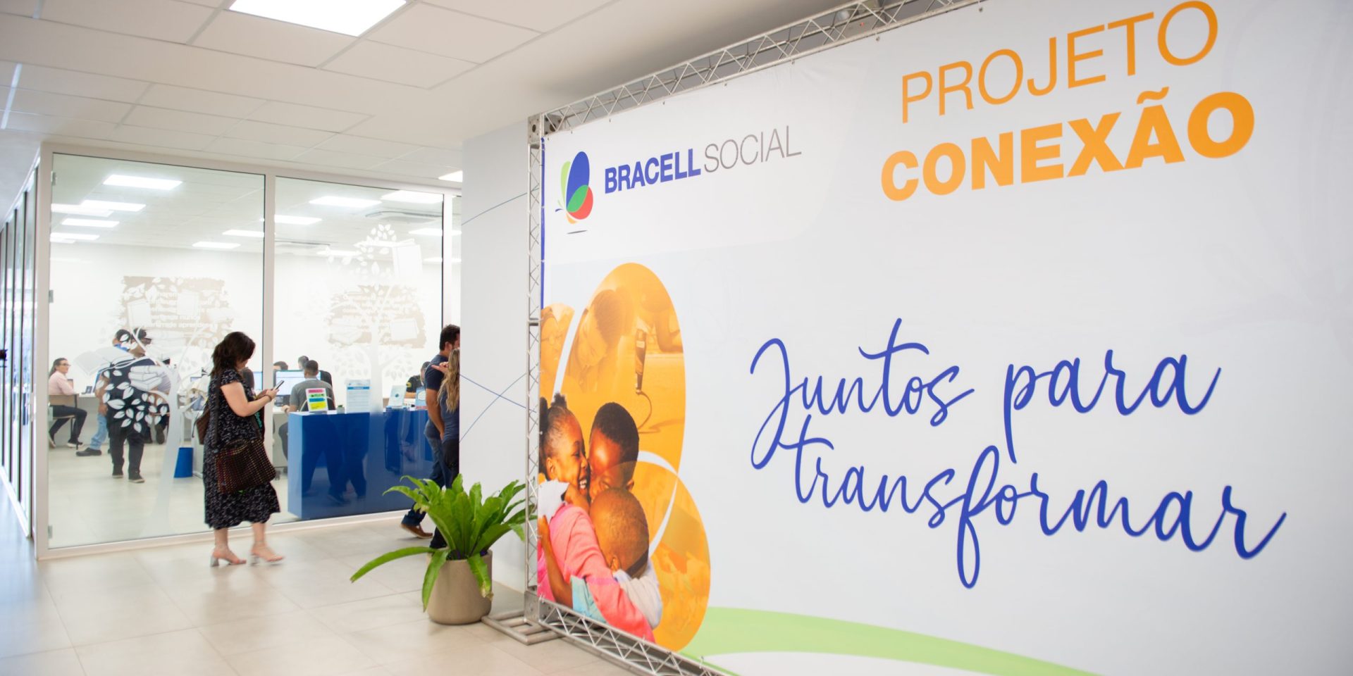 Painel do Projeto Conexão da Bracell Social em espaço de eventos, com participantes ao fundo durante atividade voltada ao fortalecimento de organizações sociais.