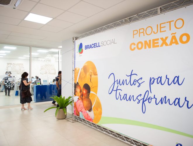 Painel do Projeto Conexão da Bracell Social em espaço de eventos, com participantes ao fundo durante atividade voltada ao fortalecimento de organizações sociais.