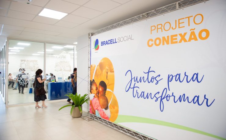 Painel do Projeto Conexão da Bracell Social em espaço de eventos, com participantes ao fundo durante atividade voltada ao fortalecimento de organizações sociais.