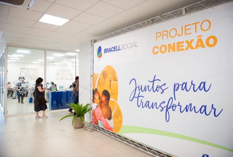 Painel do Projeto Conexão da Bracell Social em espaço de eventos, com participantes ao fundo durante atividade voltada ao fortalecimento de organizações sociais.