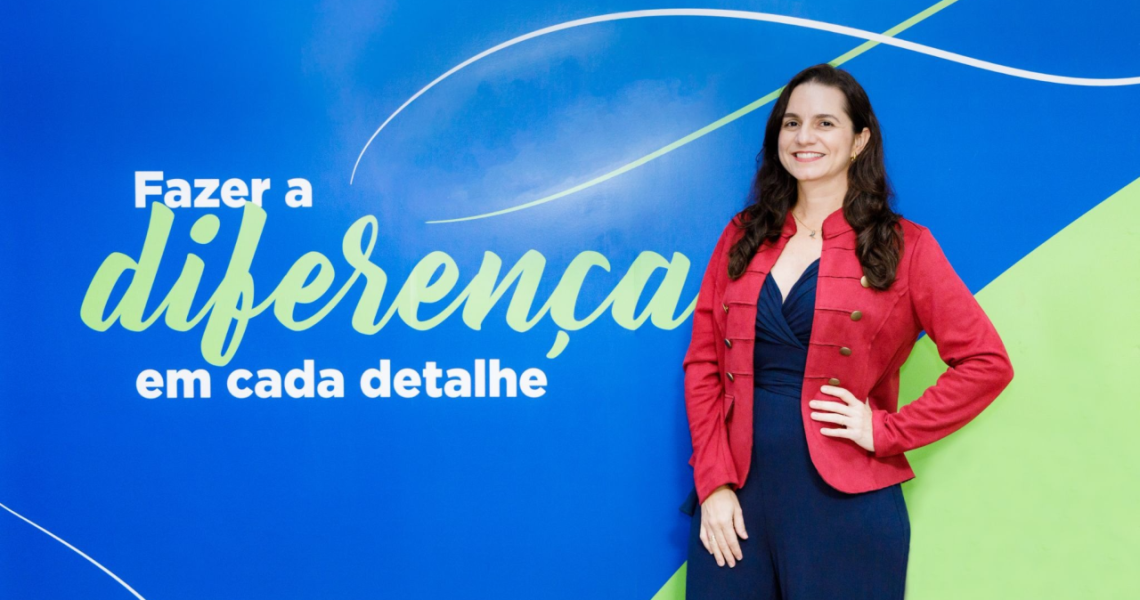 Pessoa posa diante de painel azul com a frase “Fazer a diferença em cada detalhe”