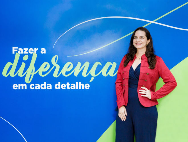 Pessoa posa diante de painel azul com a frase “Fazer a diferença em cada detalhe”