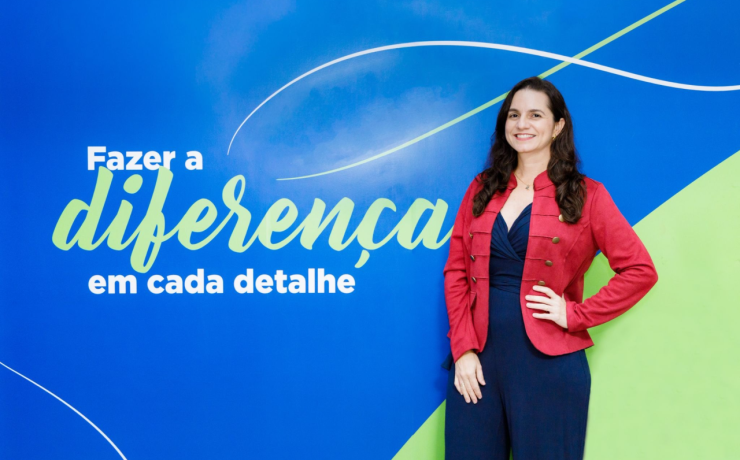 Pessoa posa diante de painel azul com a frase “Fazer a diferença em cada detalhe”