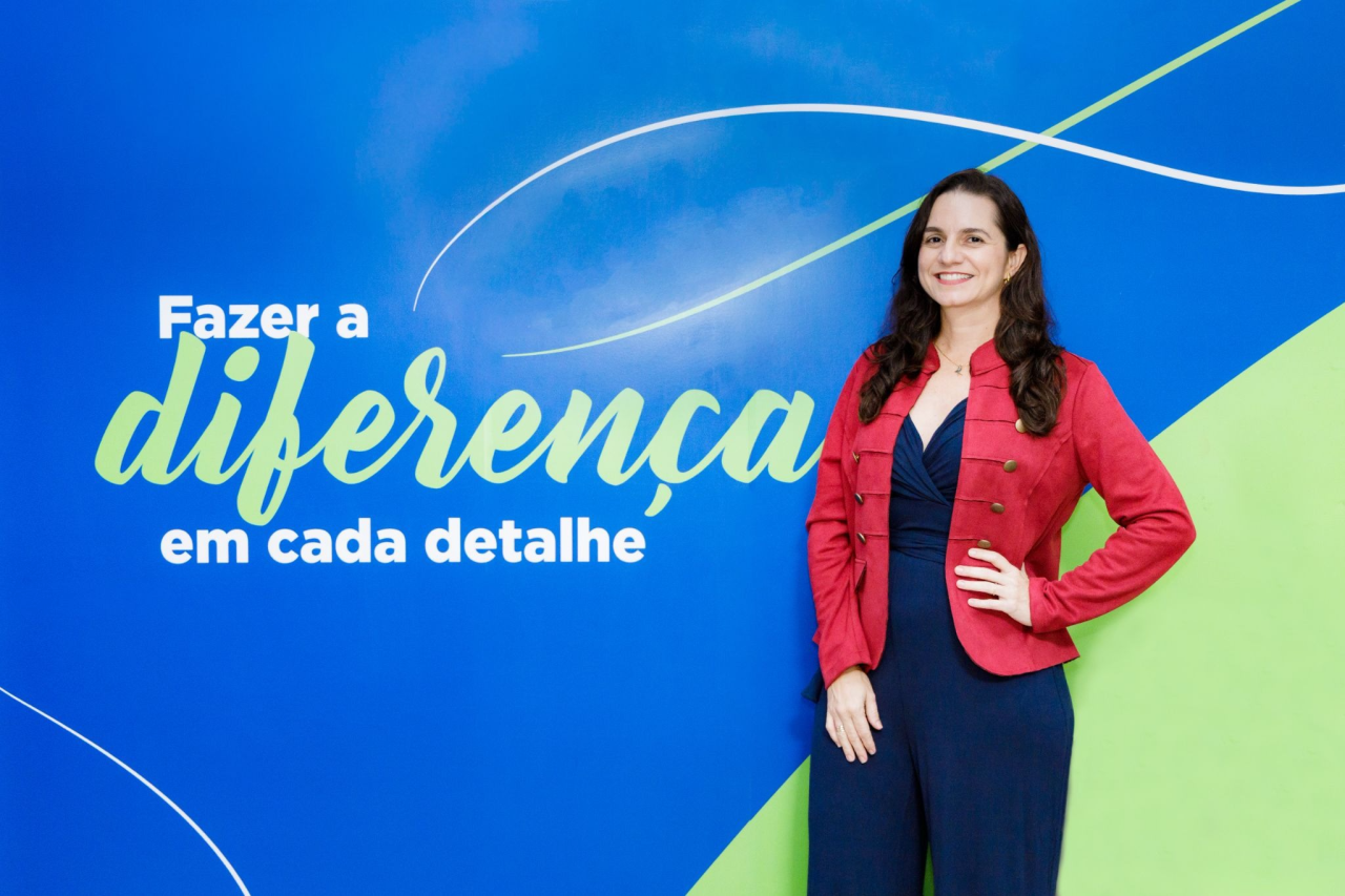 Pessoa posa diante de painel azul com a frase “Fazer a diferença em cada detalhe”