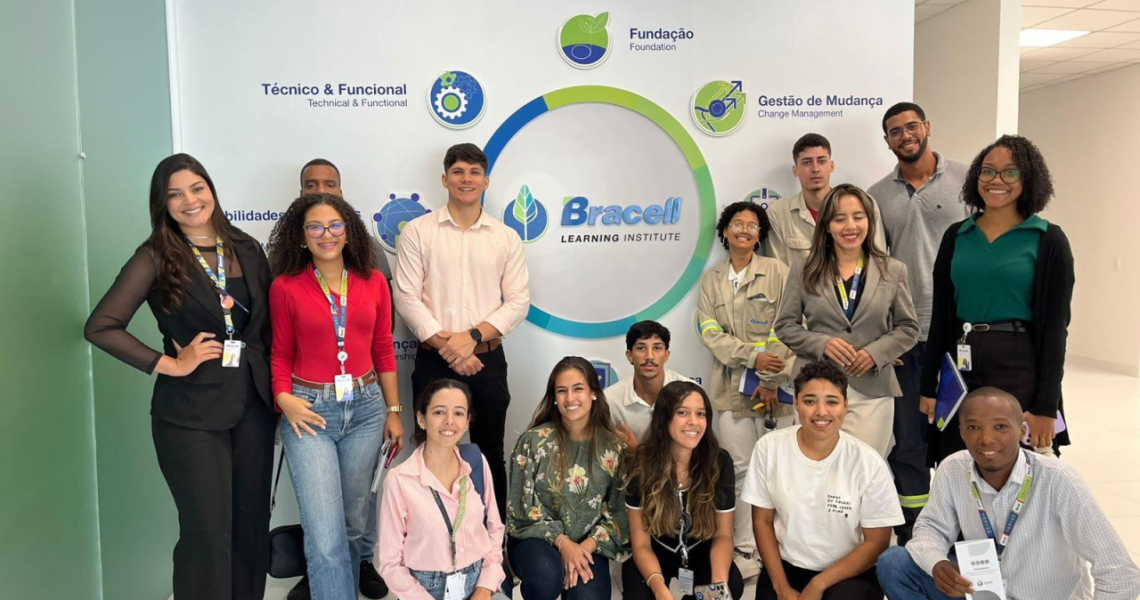 Grupo de participantes reunido em área interna da empresa diante de painel institucional da Bracell.