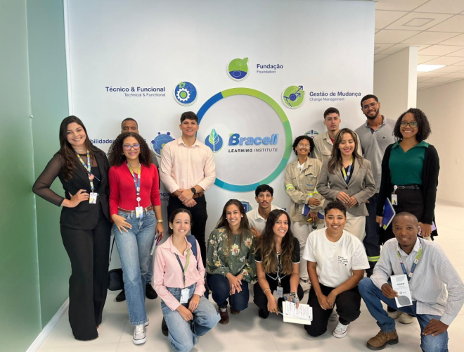 Grupo de participantes reunido em área interna da empresa diante de painel institucional da Bracell.