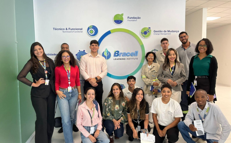 Grupo de participantes reunido em área interna da empresa diante de painel institucional da Bracell.