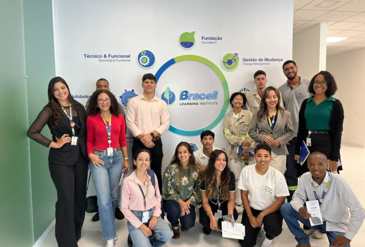 Grupo de participantes reunido em área interna da empresa diante de painel institucional da Bracell.