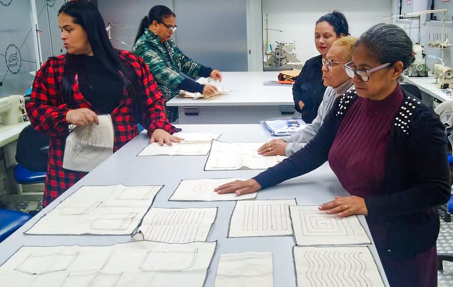 Participantes realizam atividades práticas em curso de costura, com moldes distribuídos sobre mesa de trabalho.