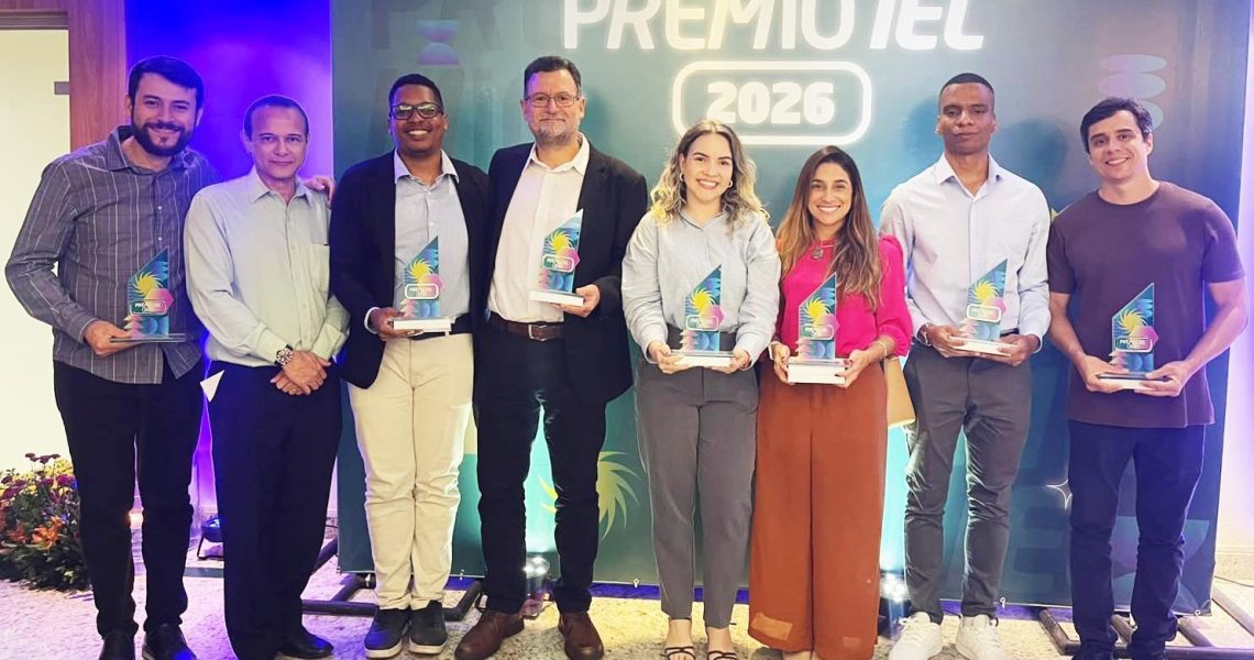 Equipe posa com troféus durante cerimônia do Prêmio IEL 2026 em frente ao painel oficial do evento.