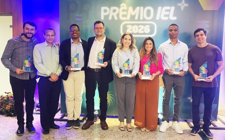 Equipe posa com troféus durante cerimônia do Prêmio IEL 2026 em frente ao painel oficial do evento.
