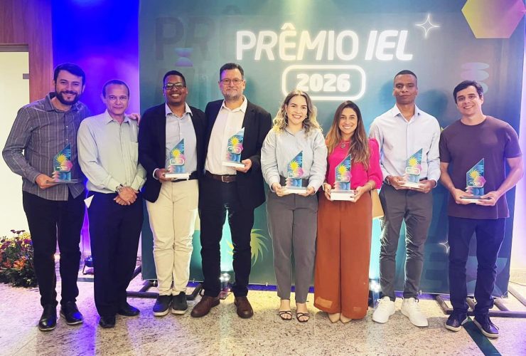 Equipe posa com troféus durante cerimônia do Prêmio IEL 2026 em frente ao painel oficial do evento.